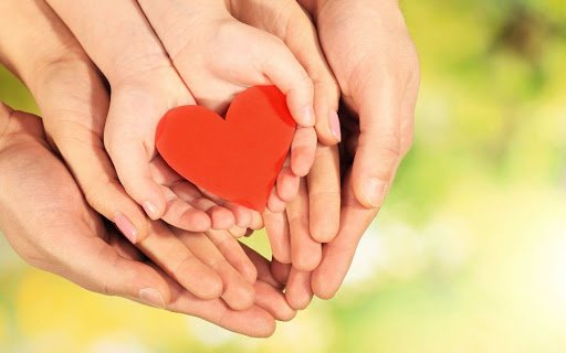 Manos de una familia sosteniendo un corazón rojo, representando todo el amor, paciencia y apoyo en el proceso de recuperación de las adicciones y sanidad interior.