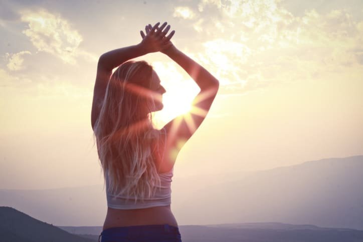Mujer levantando los brazos hacia el sol al amanecer en un paisaje natural, representando libertad, fe, orden interior y esperanza en medio del proceso de recuperación emocional y espiritual.