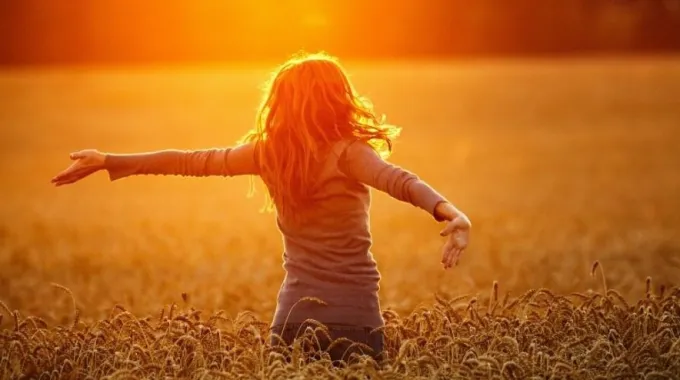 Niña con los brazos abiertos mirando al cielo al atardecer, transmitiendo esperanza, paz interior y conexión espiritual con la naturaleza como su refugio.