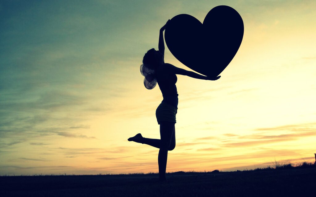 Silueta de una mujer al atardecer sosteniendo un gran corazón, simbolizando la sanidad interior, la esperanza y el amor vital 