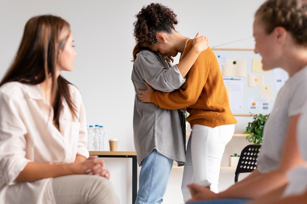 Personas en un entorno de tratamiento y recuperación de adicciones se brindan apoyo emocional mediante un abrazo, reflejando acompañamiento, empatía y esperanza en el proceso de sanación y restauración familiar.